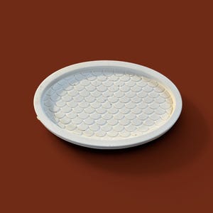 Peut inclure: Un plateau décoratif ovale blanc avec un motif en écailles à l'intérieur. Le plateau est fait d'un matériau solide et repose sur une surface marron. Le design est simple et élégant.