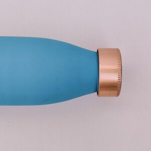 May include: A close-up of a teal water bottle with a copper-coloured cap. The bottle has a smooth, matte finish. The cap is a solid copper colour with a ridged texture.