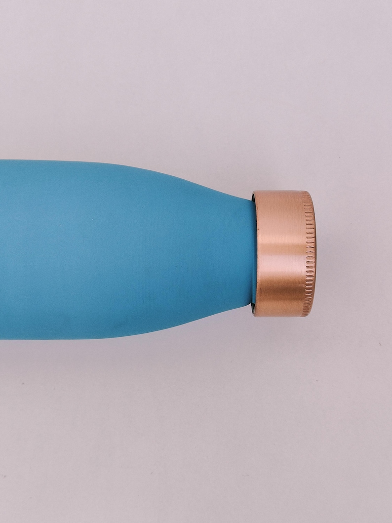 May include: A close-up of a teal water bottle with a copper-coloured cap. The bottle has a smooth, matte finish. The cap is a solid copper colour with a ridged texture.