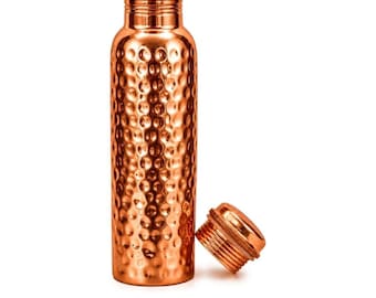 May include: A cylindrical copper water bottle with a polished, hammered texture across its surface. The bottle features a narrow neck and a matching screw-top lid, which is shown detached and resting beside the base of the bottle.