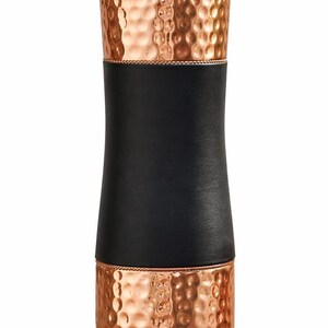 May include: A copper-colored water bottle with a hammered texture. The bottle has a black leather band around the middle. The top and bottom sections are copper, and the lid is also copper-colored.
