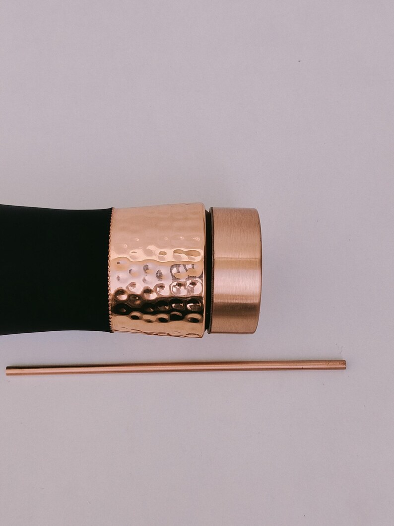 May include: A black water bottle with a hammered copper band and cap, and a copper straw. The bottle has a sleek design, with a textured band adding visual interest. The straw is thin and straight.