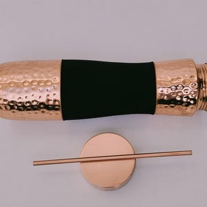 May include: A copper-colored water bottle with a hammered texture and a black band. The bottle is accompanied by a matching copper-colored lid and a straw. The bottle has a screw-on top.
