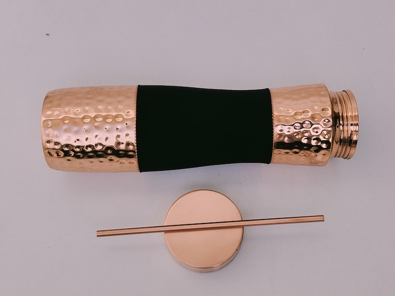 May include: A copper-colored water bottle with a hammered texture and a black band. The bottle is accompanied by a matching copper-colored lid and a straw. The bottle has a screw-on top.