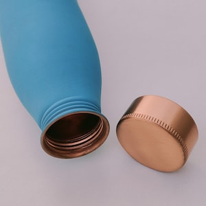 May include: A light blue insulated water bottle with a copper-coloured screw-on lid. The bottle is cylindrical and has a smooth, matte finish. The lid is detached, revealing the bottle's opening.