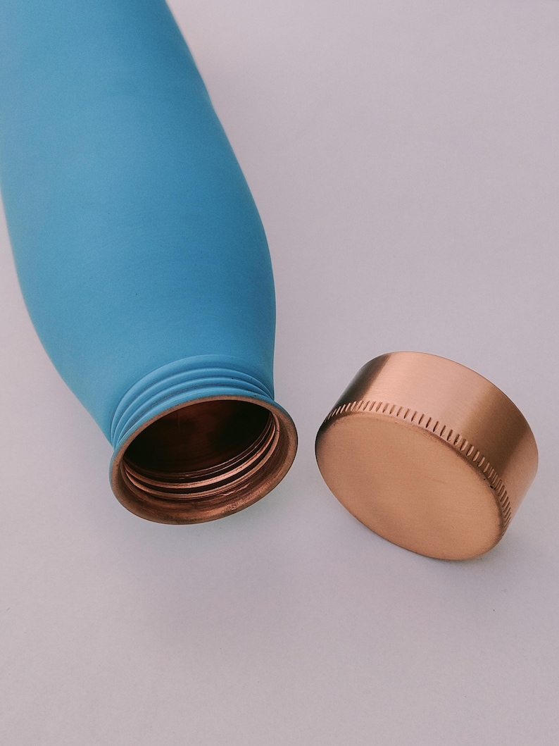 May include: A light blue insulated water bottle with a copper-coloured screw-on lid. The bottle is cylindrical and has a smooth, matte finish. The lid is detached, revealing the bottle's opening.