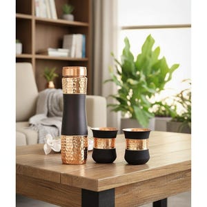 May include: A copper and black insulated water bottle and two matching cups sit on a wooden table. The bottle has a hammered copper top and bottom with a black center. The cups are black with copper bands.