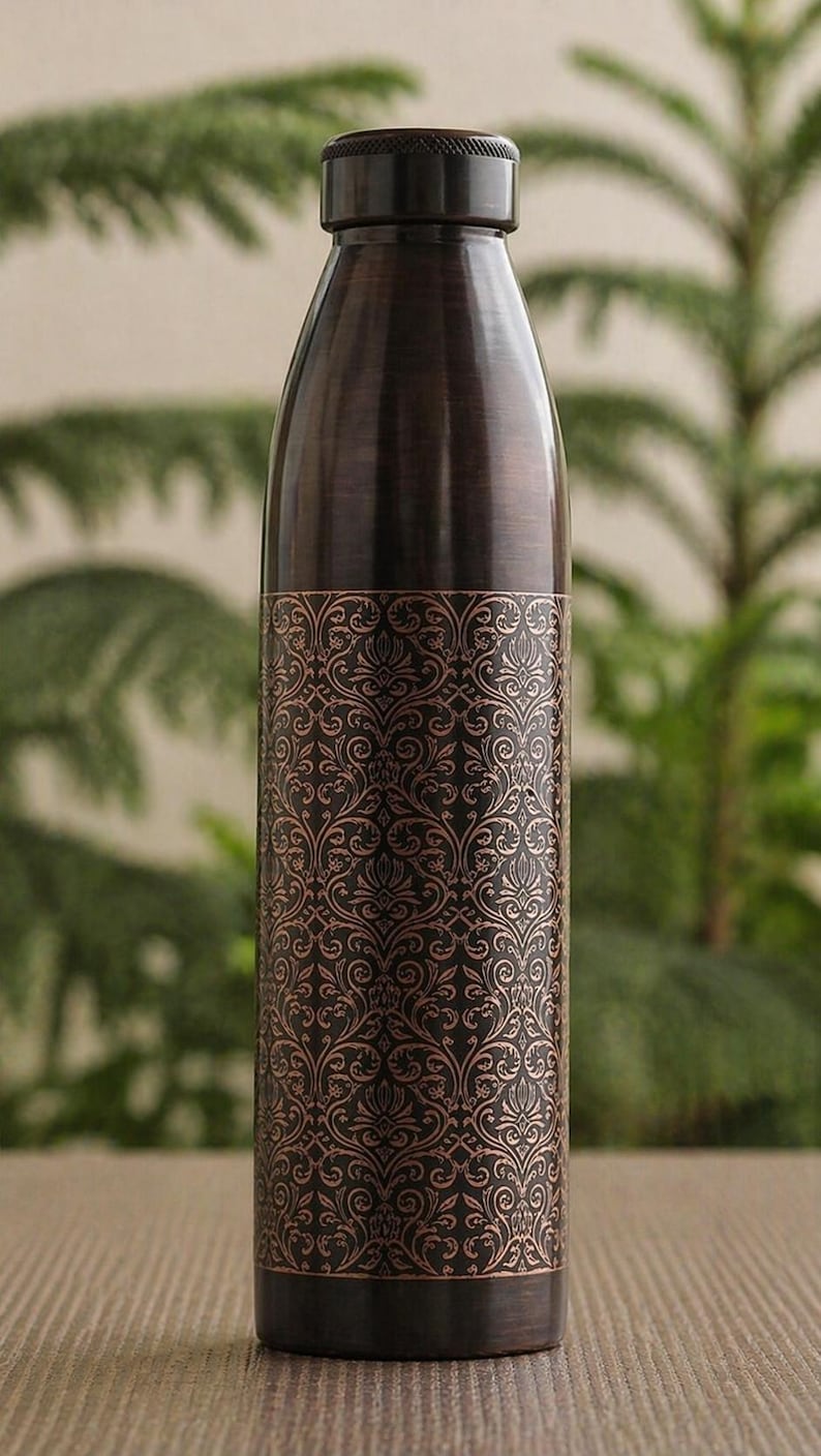 May include: A copper-coloured water bottle with a decorative floral pattern. The bottle has a dark cap and base, and the patterned section is in a lighter copper hue. The bottle is designed to keep beverages cold or hot.