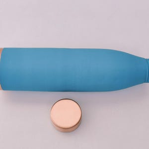 May include: A turquoise water bottle with a copper-coloured rim and a matching copper-coloured lid. The bottle is cylindrical with a slightly textured surface. The lid is round and sits next to the bottle.