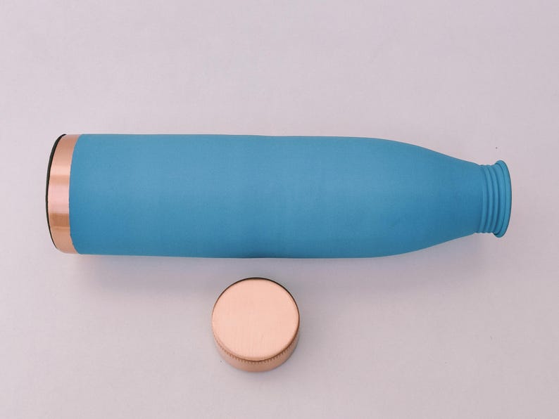 May include: A turquoise water bottle with a copper-coloured rim and a matching copper-coloured lid. The bottle is cylindrical with a slightly textured surface. The lid is round and sits next to the bottle.