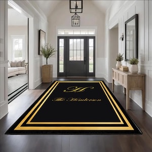 Puede incluir: Alfombra de bienvenida rectangular negra con borde dorado y el nombre "The Henderson" en escritura dorada. La alfombra está colocada en la entrada de una casa con suelo de madera oscura y paredes blancas.