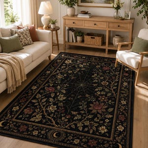 May include: A rectangular area rug featuring a black background with a central spiderweb design surrounded by intricate floral patterns in muted tones of red, green, and gold, finished with a decorative border containing moon and sun motifs.