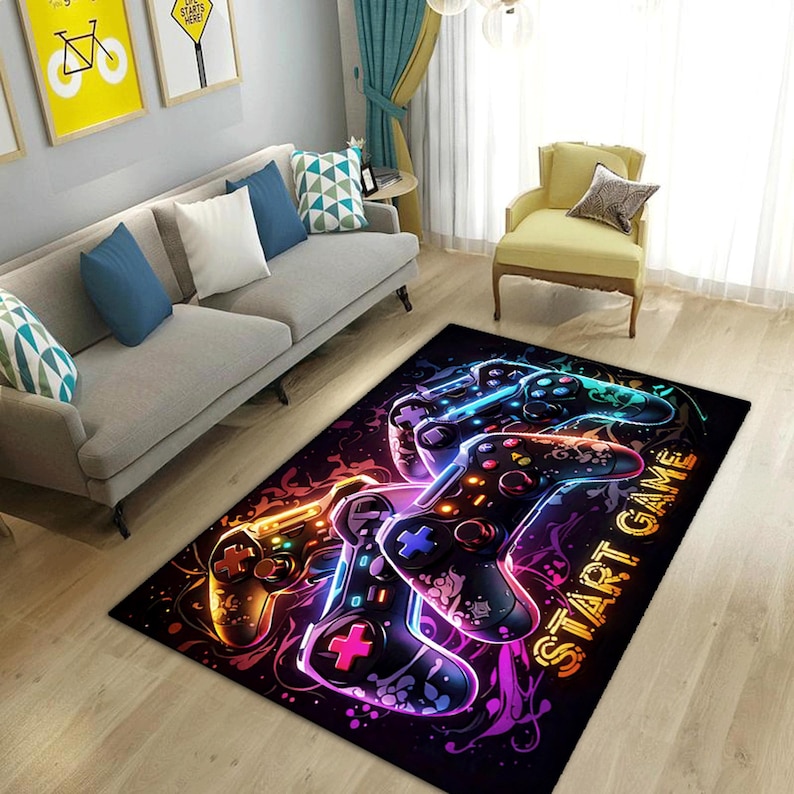Puede incluir: Una alfombra rectangular con fondo negro y un estampado gr&aacute;fico vibrante de varios mandos de videojuegos en colores ne&oacute;n. El dise&ntilde;o incluye patrones abstractos en espiral y el texto START GAME en letras de color amarillo.