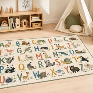 May include: A rectangular area rug featuring a colorful alphabet design from A to Z. Each letter is paired with a corresponding animal illustration and its name printed in black text. The rug has a light cream background and a dark green border.