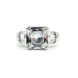 May include: A silver-toned ring featuring a large, square-cut clear center stone held by four prongs. The band is accented on each side by a row of three rectangular baguette-cut clear stones, set horizontally within the polished metal band.