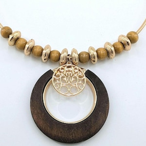 May include: A gold-toned necklace with a wooden pendant. The pendant is a dark brown wooden circle with a gold-toned inner ring and a gold filigree design. The necklace also features wooden beads and gold-toned accents.