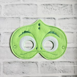 May include: A lime green felt mask with white eye openings and a stitched design. The mask has a whimsical design with a small, pointed top and decorative elements above the eyes. The mask is designed for costume or play.