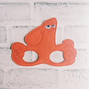 May include: An orange felt mask shaped like an octopus with two eye holes. The mask features embroidered details including a prominent head section, curled tentacles on the sides, and two blue and white eyes positioned near the top center.