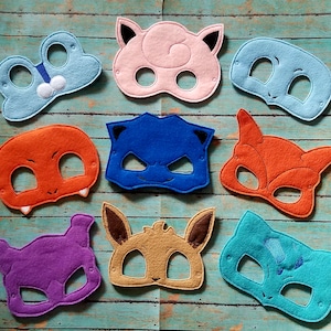 May include: A collection of colorful felt masks in various shapes and colors, including blue, pink, orange, purple, brown, and teal. Each mask features eye holes and is designed with unique character features.