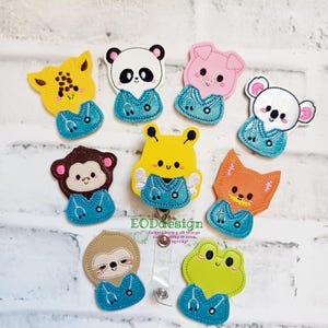 May include: A collection of embroidered animal badge reels, including a giraffe, panda, pig, koala, monkey, fox, sloth, and frog. Each animal wears a blue medical uniform with a stethoscope. The badge reels are attached to a clear plastic clip.