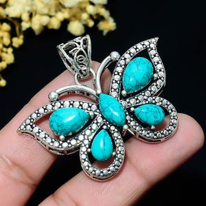 May include: A silver-toned butterfly pendant with turquoise gemstones. The pendant features a detailed design with a central body and two wings, each adorned with multiple turquoise stones. The butterfly pendant is held in a hand.