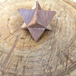 Op de afbeelding: Een houten geometrische sterpuzzel met driehoekige vlakken. De puzzel heeft een warme bruine kleur en ligt op een lichtbruin, getextureerd houten oppervlak. De ster heeft een driedimensionaal ontwerp.