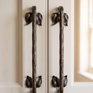 May include: Two vertical door handles made of dark bronze-toned metal with a textured, branch-like surface. Each handle features decorative metal leaves at the top and bottom mounting points. A matching dark bronze keyhole plate is mounted below.