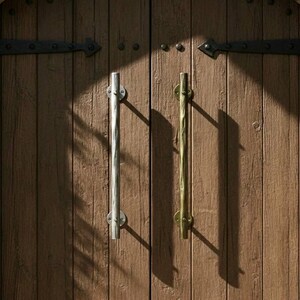Könnte beinhalten: Nahaufnahme einer Holztür mit Steinbogen. Die Tür besteht aus vertikalen Holzbrettern mit Metallscharnieren und dekorativen Beschlägen. Sie hat zwei lange, vertikale Griffe, einen silbernen und einen goldenen.