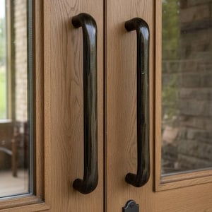 May include: Close-up of a wooden door with two dark, curved handles. The door is made of light brown wood with visible grain. A black, ornate door lock is also visible, adding a touch of classic design.