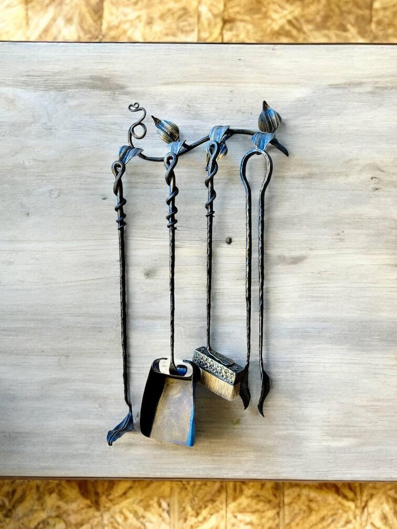 May include: A black wrought iron fireplace tool set with a decorative top featuring blue and gold accents. The set includes a poker, shovel, brush, and a tool with a looped handle. The tools hang on a matching holder.