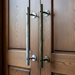 以下が含まれることがあります： 2つの垂直な金属製のドアプルが付いた木製のドアのクローズアップ。ドアプルは円筒形で、円形のプレートに取り付けられています。ドアは木製で木目がはっきりと見え、プルは金属仕上げです。