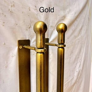 K&ouml;nnte beinhalten: Ein goldfarbenes T&uuml;rgriff-Set aus Metall mit zwei vertikalen zylindrischen Stangen und abgerundeten, kugelf&ouml;rmigen Endst&uuml;cken an der Oberseite. Jede Stange ist mit einer sichtbaren Schraube an einer rechteckigen Montageplatte befestigt. Der Text Gold steht dar&uuml;ber.