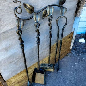 May include: A decorative fireplace tool set with a leaf and vine design. The set includes a poker, shovel, brush, and a tool with a curved end. The tools are made of dark metal with gold accents.