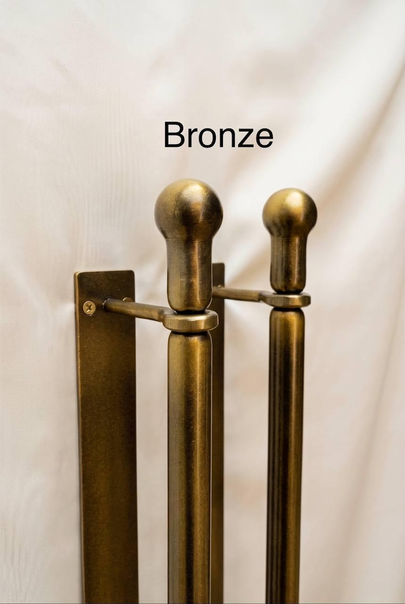 K&ouml;nnte beinhalten: Ein bronzefarbener Handtuchhalter aus Metall zur Wandmontage mit zwei vertikalen Stangen und abgerundeten Endst&uuml;cken. Die Halterung besteht aus einer rechteckigen Montageplatte mit einer sichtbaren Schraube. Das Wort Bronze steht dar&uuml;ber.