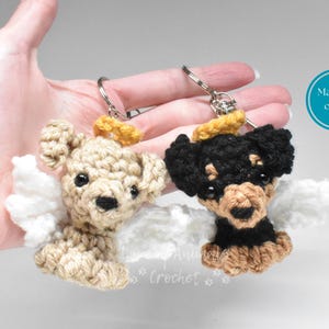 May include: Two handmade crochet dog keychains, one tan and one black and tan, each with white wings and a yellow halo. The keychains are held up by a hand. The text "Made to order" is in a blue circle.