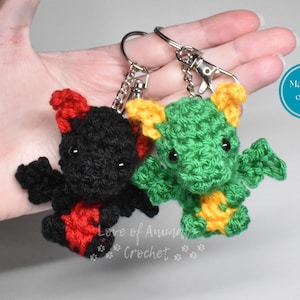 May include: Two handmade crochet dragon keychains. One dragon is black with red accents, the other is green with yellow accents. Both have silver key rings and lobster clasps. The text "Love of Animals Crochet" is visible.