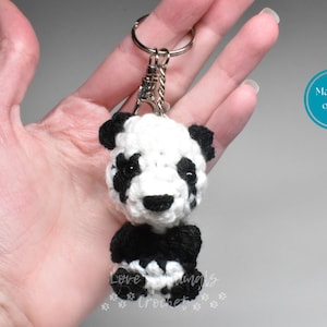 May include: A handmade crochet panda bear keychain. The panda is white with black accents on the ears, eyes, and limbs. The keychain is attached to a silver-colored metal ring. The text "Made to order" is in a blue circle.