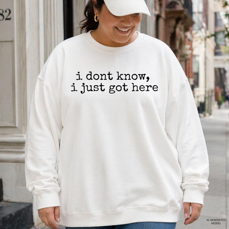 Puede incluir: Una sudadera blanca de manga larga con cuello redondo y el texto negro "i dont know, i just got here" impreso en el pecho. La prenda tiene un corte relajado con pu&ntilde;os y dobladillo acanalados, lo que le confiere un aspecto sencillo y limpio.