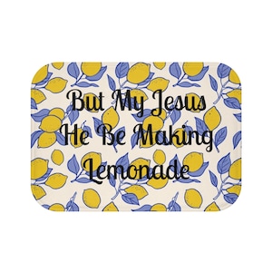 Puede incluir: Alfombra de baño rectangular con fondo crema y un estampado de limones amarillos y hojas azules. La alfombra presenta el texto "But My Jesus He Be Making Lemonade" en escritura negra.