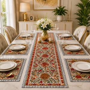 May include: A dining table set featuring a long rectangular table runner and six matching placemats, all decorated with a vibrant floral pattern in shades of red, orange, and green on a light background, with white plates and gold cutlery.