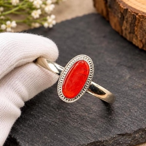 May include: A silver-toned cuff bracelet featuring a central oval-shaped, vibrant red stone. The stone is encased in a decorative, textured silver-toned bezel with a beaded border. The band of the bracelet is smooth, polished, and metallic.