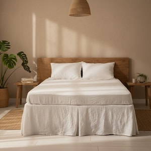 Pode incluir: Uma cena de quarto com uma cama com roupa de cama branca e um cobertor listrado. A cama tem uma cabeceira de madeira e é ladeada por pequenas mesas laterais de madeira. Uma grande planta em vaso e uma luminária pendente tecida também são visíveis.