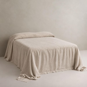 May include: A bed covered with a solid light beige bedspread that drapes over the sides and foot of the frame. The fabric has a visible textured weave and a matte finish, creating a uniform appearance across the entire surface of the bedding.