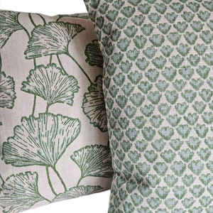 Op de afbeelding: Twee decoratieve kussens met een licht beige achtergrond en groene patronen. Een kussen heeft een herhalend patroon van kleine groene bladeren. Het andere kussen heeft een groter groen bladpatroon.