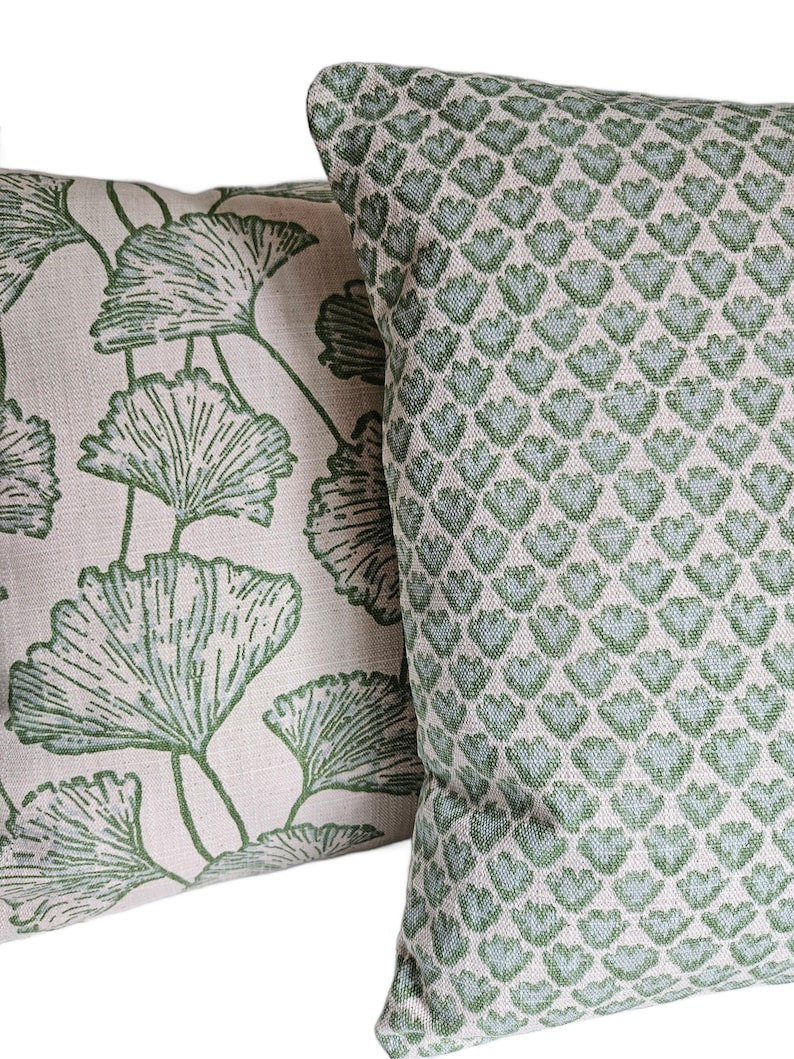 Op de afbeelding: Twee decoratieve kussens met een licht beige achtergrond en groene patronen. Een kussen heeft een herhalend patroon van kleine groene bladeren. Het andere kussen heeft een groter groen bladpatroon.