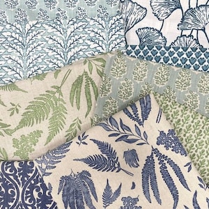 Op de afbeelding: Assortiment van stofstalen met verschillende bloemen- en bladpatronen in tinten blauw, groen en wit. De stoffen zijn in een gelaagde weergave gerangschikt, waardoor de verschillende texturen en ontwerpen worden getoond.