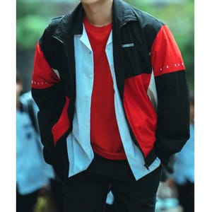 May include: A colour-blocked jacket in black, red, and white with the word "GARMENTS" printed on the upper chest. The jacket is worn over a red t-shirt and a white button-down shirt. The person is also wearing black trousers.