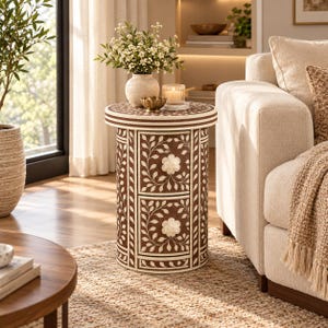 May include: A cylindrical side table featuring a brown and white floral inlay pattern. The table has two stacked drawers, each adorned with a central flower-shaped knob and intricate vine motifs covering the exterior surface.