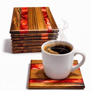 Könnte beinhalten: Holzuntersetzer mit roten Harzeinlagen, neben einer weißen Tasse mit dampfendem Kaffee. Die rechteckigen Untersetzer haben eine natürliche Holzmaserung. Das rote Harz setzt einen auffälligen Kontrast. Die Untersetzer sind ca. 10 cm groß.