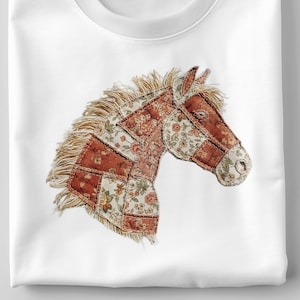 May include: White crew neck t-shirt with a patchwork horse head design. The horse head is made from floral and patterned fabrics in red, cream, and brown. The mane is a light tan colour.